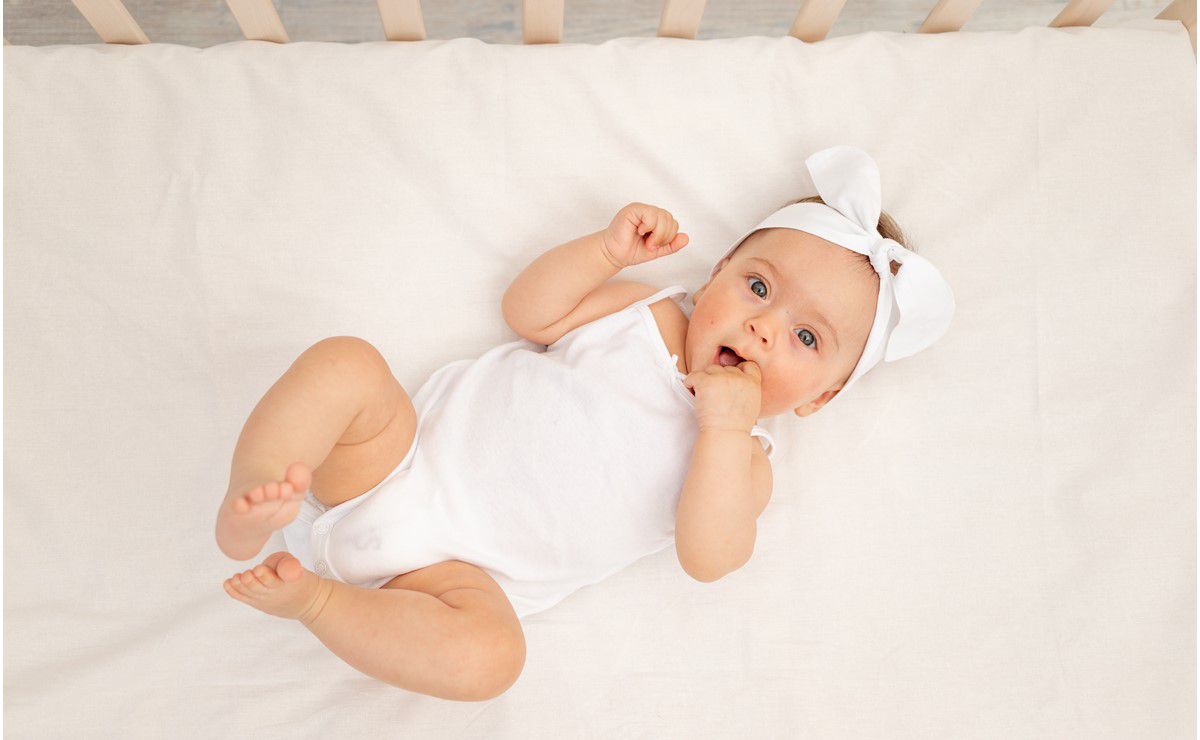 beba obučena u belo leži na krevetu