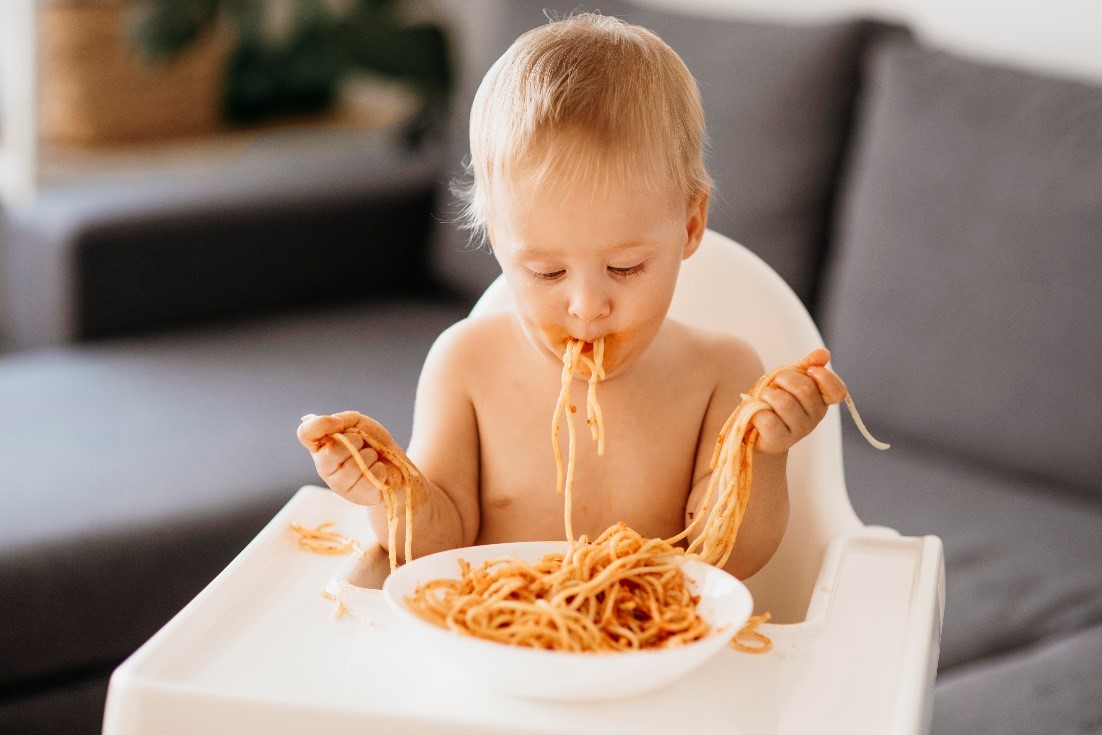 beba koja sedi u stolici i umusavila se jedući špagete 