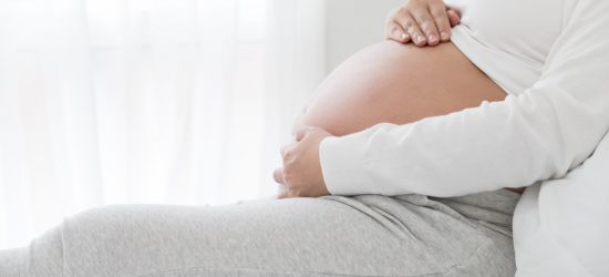 trudnica u poodmakloj trudnoći na krevetu drži ruke na stomaku